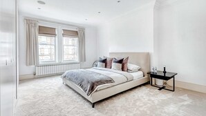 A bedroom with a bed, a bedside table, a radiator, and a window with curtains.
