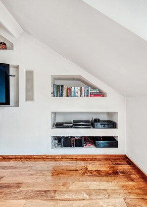 A modern interior with a sloped ceiling, wooden flooring, and built-in shelving units containing books and electronic devices.