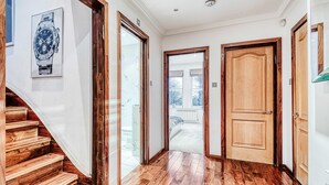 A hallway with wooden flooring, a staircase, and a door leading to a balcony.