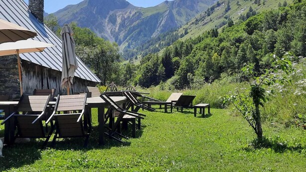 A rustic outdoor seating area with wooden tables and chairs, a stone chimney, and a view of mountains. - Ground floor, parking, tv, ski locker, 61m², Valloire (Valloire)