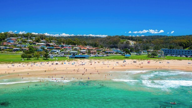 A beach with clear turquoise waters, a sandy shore, and a backdrop of residential buildings. - Minutes to Malua Bay Beach | Sunset Vista Retreat (Malua Bay)