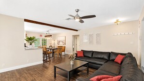 A modern living room with a sectional sofa, a dining area, and a kitchen in the background. - Wonderful 4BR & 3BA Villa Heated Pool near Beach (Hollywood)