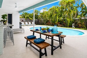 Un espace aménagé au bord de la piscine, avec une table en bois, des coussins bleus et une piscine.