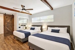 A bedroom with two beds, a ceiling fan, wooden beams, a large mirror, and a sliding barn door.