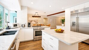 A modern kitchen with white cabinetry, stainless steel appliances, a marble countertop, and a central island with a fruit bowl. - Wonderful 4BR & 3BA Villa Heated Pool near Beach (Hollywood)