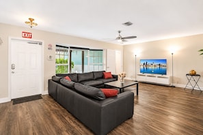 A modern living room with a sectional sofa, a flat-screen TV, and a ceiling fan.