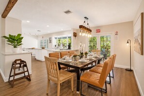Une cuisine moderne avec des meubles blancs, un coin repas avec des chaises en bois et une vue sur la verdure à l’extérieur.