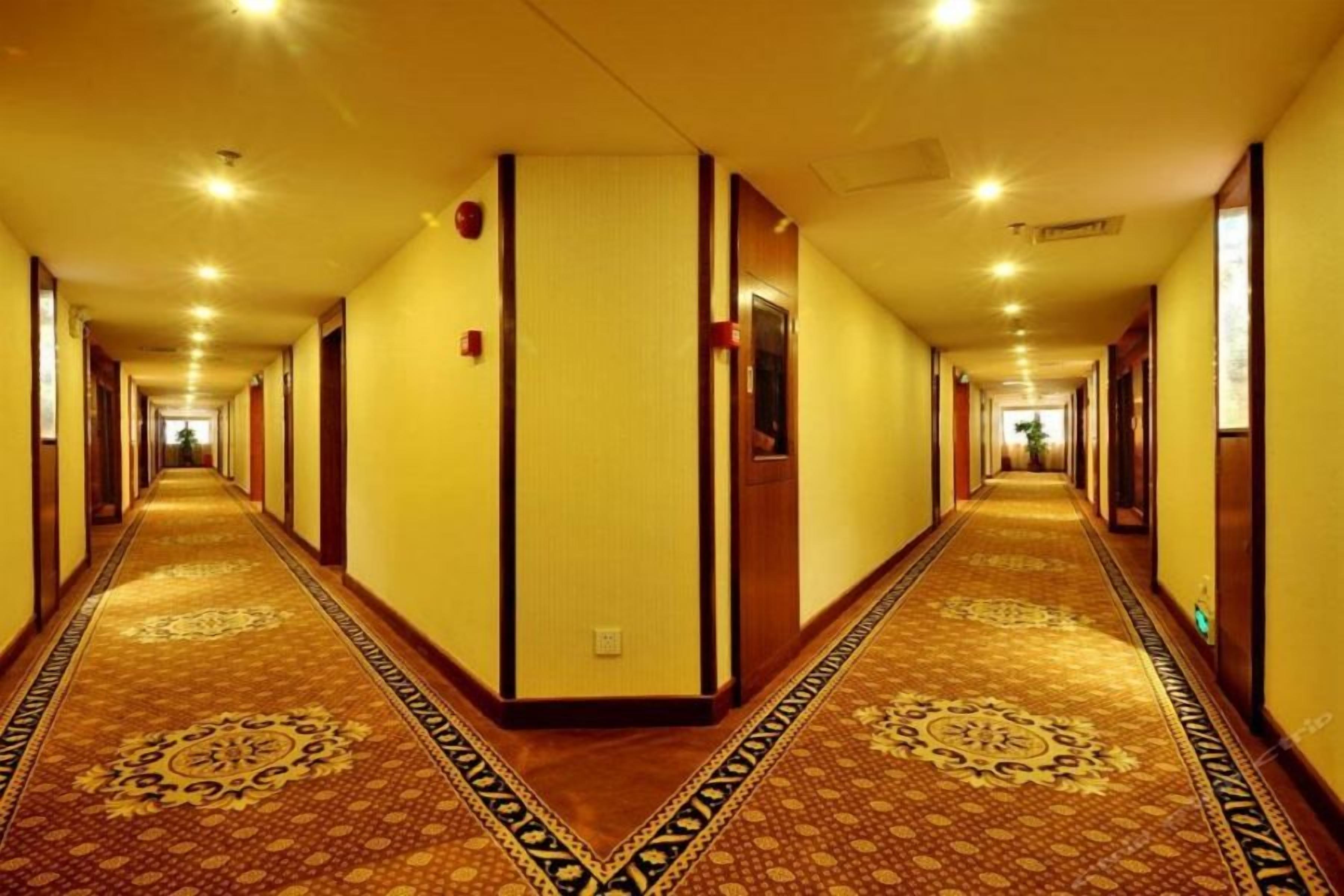 A hotel corridor with carpeted floors, wooden doors, and recessed lighting.