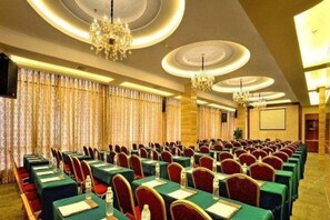 A conference room with rows of tables and chairs, chandeliers, and curtains. - Golden Diamond Hotel (Zhaoqing)