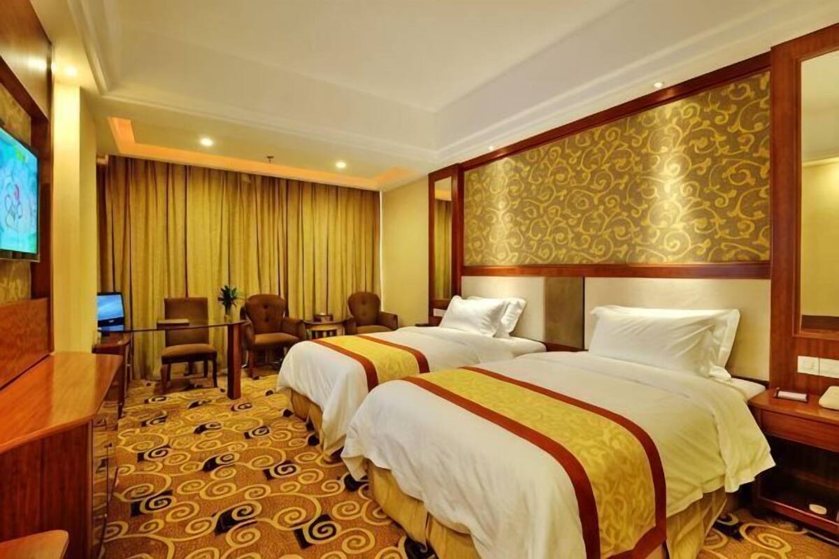 A hotel room with two beds, a desk, a chair, a TV, and a large mirror.