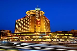 A hotel with a prominent tower and signage, surrounded by a busy street with light trails. - Golden Diamond Hotel (Zhaoqing)