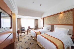Ein Hotelzimmer mit zwei Betten, einem Schreibtisch, einem Sessel und einem Fernseher.