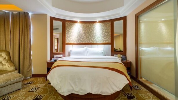 Una habitación de hotel con una cama grande, una zona de estar con una silla, una mesita de noche y un ventanal amplio.
