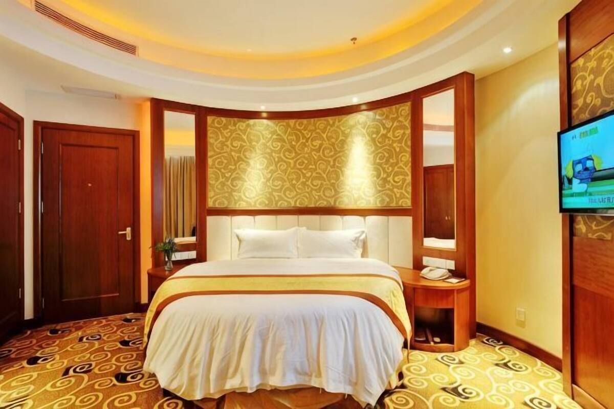 A hotel room with a large bed, a TV, a wooden headboard, and a patterned carpet.