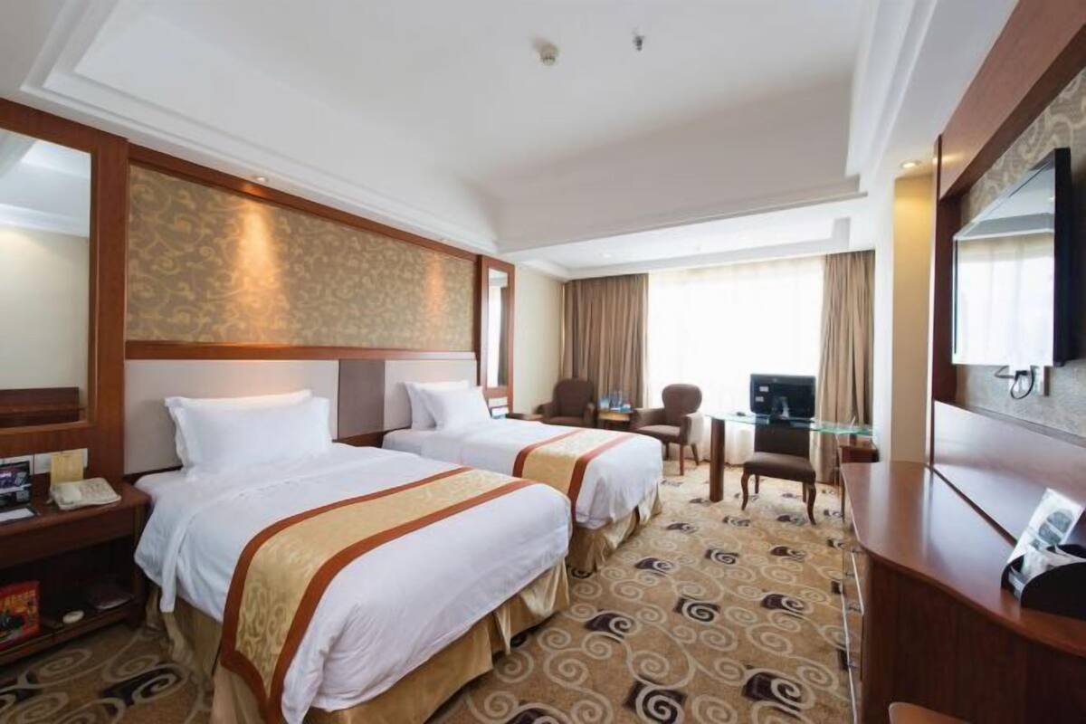 A hotel room with two beds, a desk, a chair, a television, and a patterned carpet.