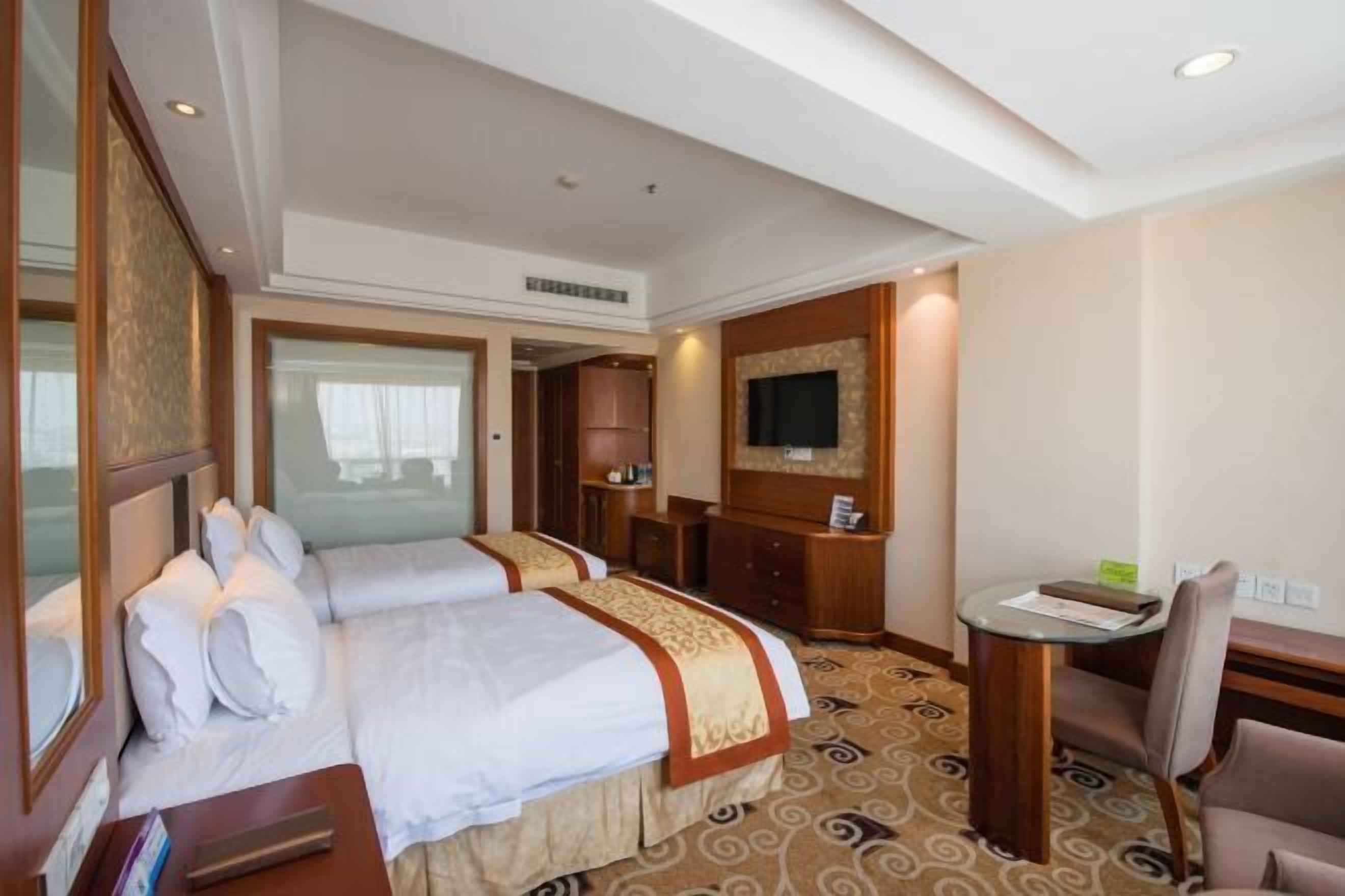 A hotel room with two beds, a desk, a chair, a television, and a patterned carpet.