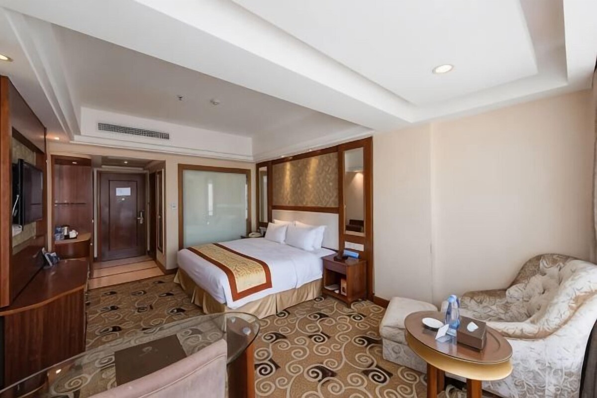 A hotel room with a large bed, a desk, a chair, and a small table.