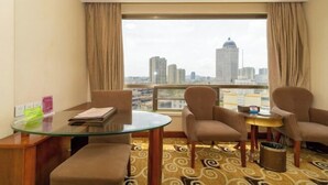 Habitación de hotel con una mesa de vidrio, dos sillas, un sofá, vistas a la ciudad y una alfombra estampada.
