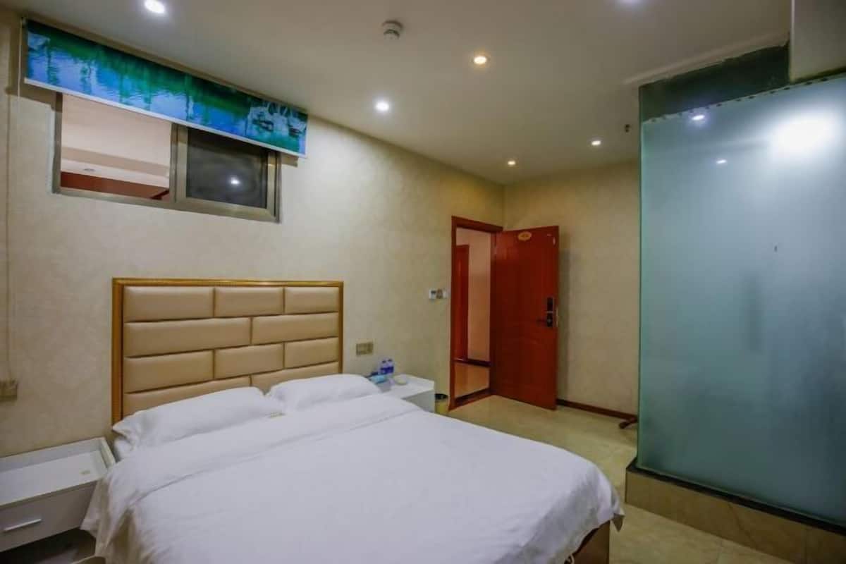Habitación de hotel con cama, mesita de noche, televisor montado en la pared, puerta y panel de vidrio esmerilado.