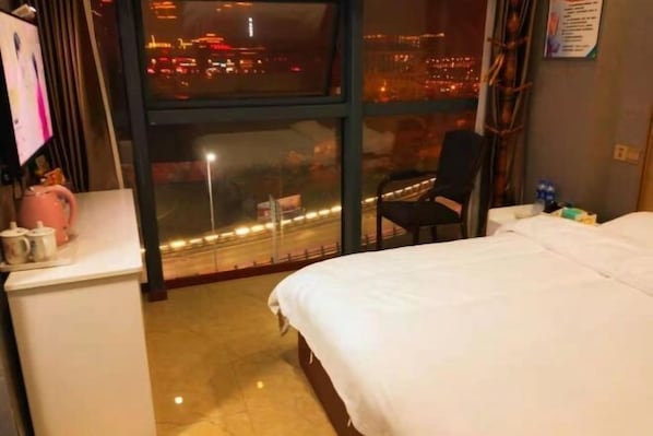 Une chambre d’hôtel avec un lit, un bureau doté d’une bouilloire, une chaise et une fenêtre donnant sur la ville.