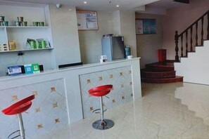 Zona de recepción con mostrador, dos taburetes rojos, una escalera y un letrero en la pared.