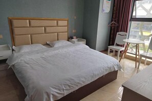 Habitació d'hotel amb un llit gran, una taula de nit, una cadira, una taula petita i vista exterior per la finestra.