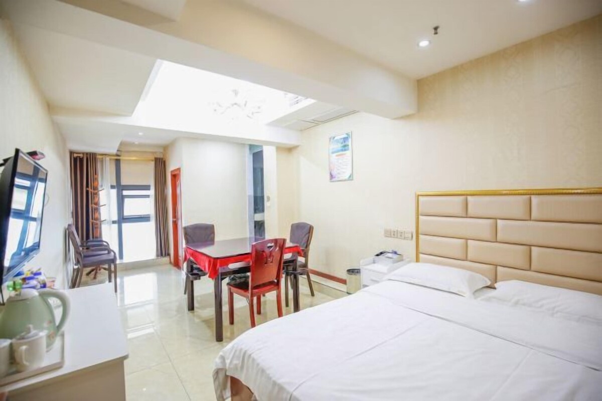 A hotel room with a bed, a desk with chairs, a small table, and a TV.