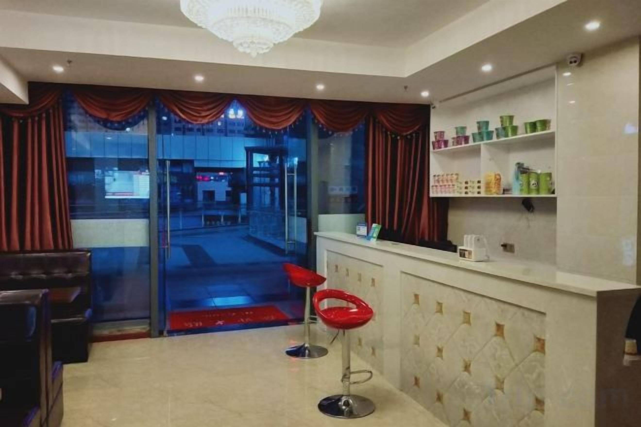 Un vestíbulo de hotel con mostrador de recepción, un taburete rojo y vistas a la calle.