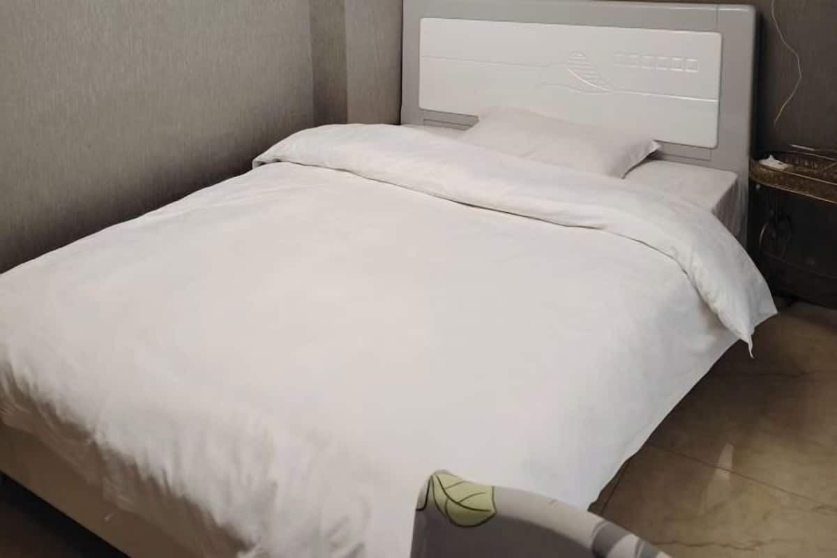Una cama bien hecha con cubrecama blanco y almohadas, cabecera gris con diseño de hojas y suelo de baldosas.