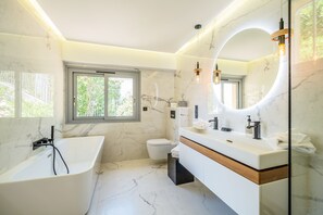 Et moderne badeværelse med et fristående badekar, en vask med spejl og et toilet.