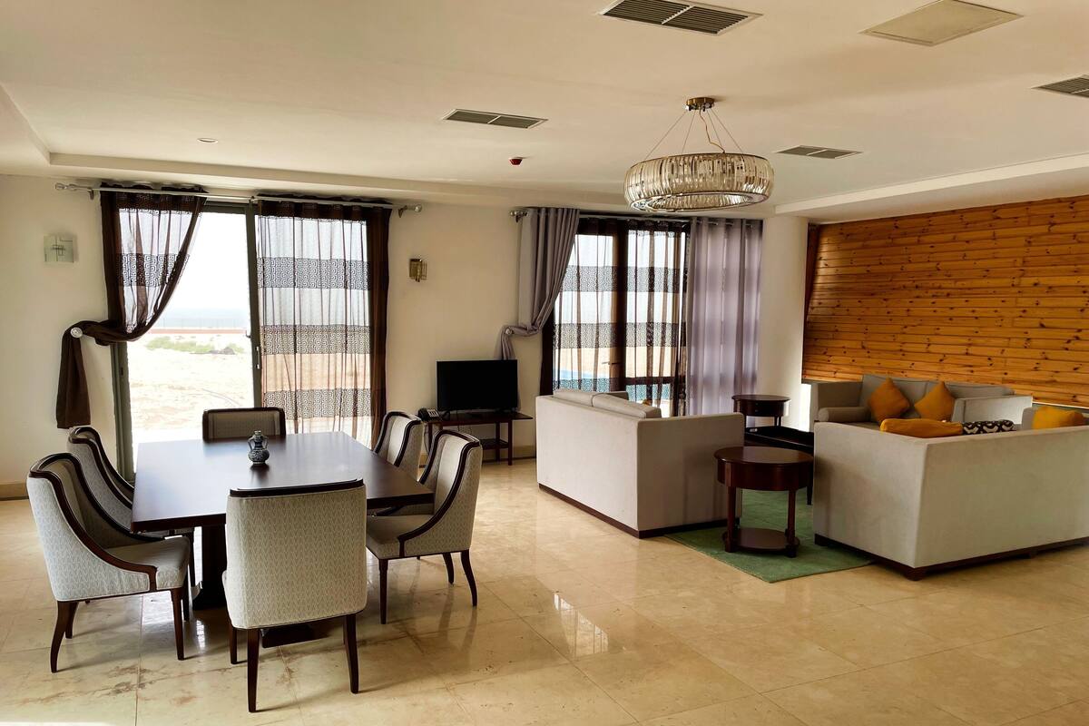 A modern living room with a dining area, a sofa set, a TV, and a wooden ceiling.
