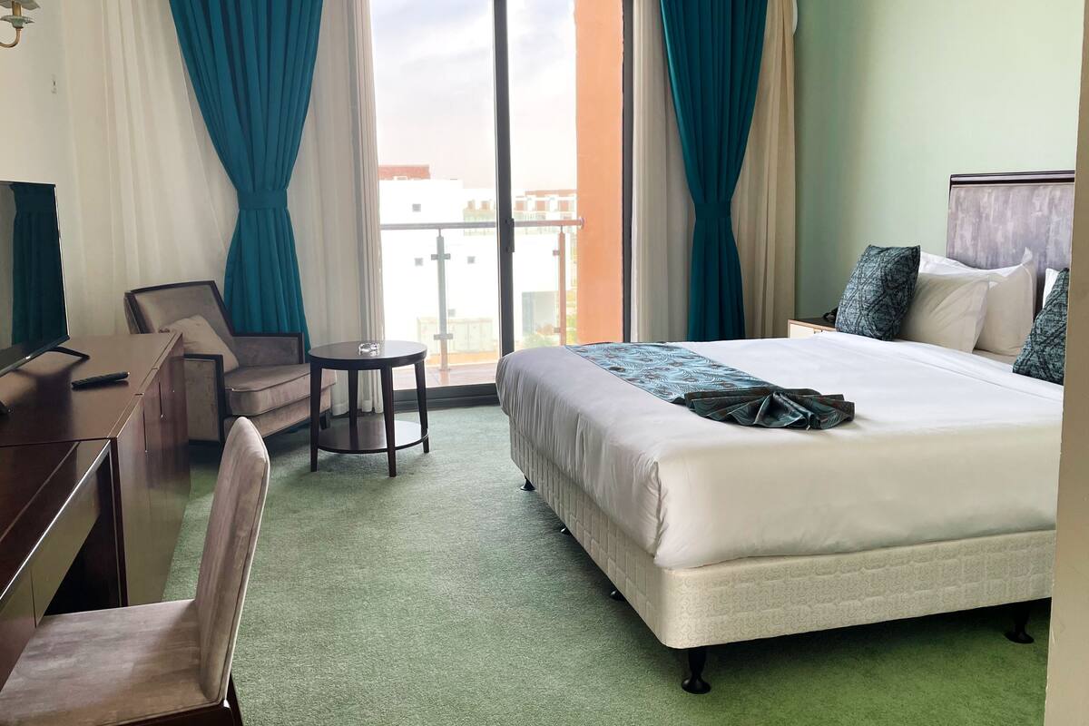 A hotel room with a bed, a desk, a chair, and a small table.