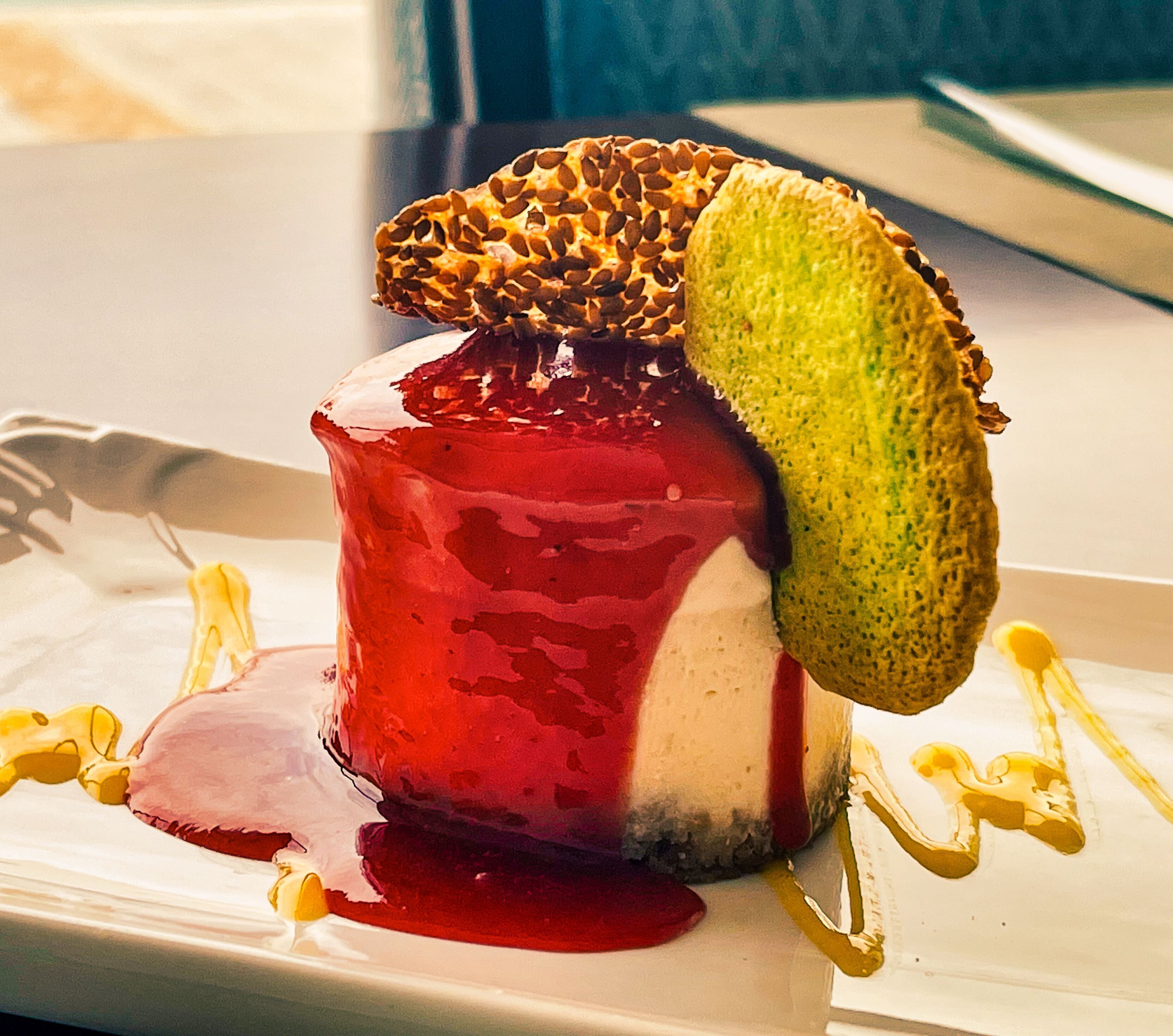 A dessert with a red sauce, a green topping, and a golden drizzle on a white plate.