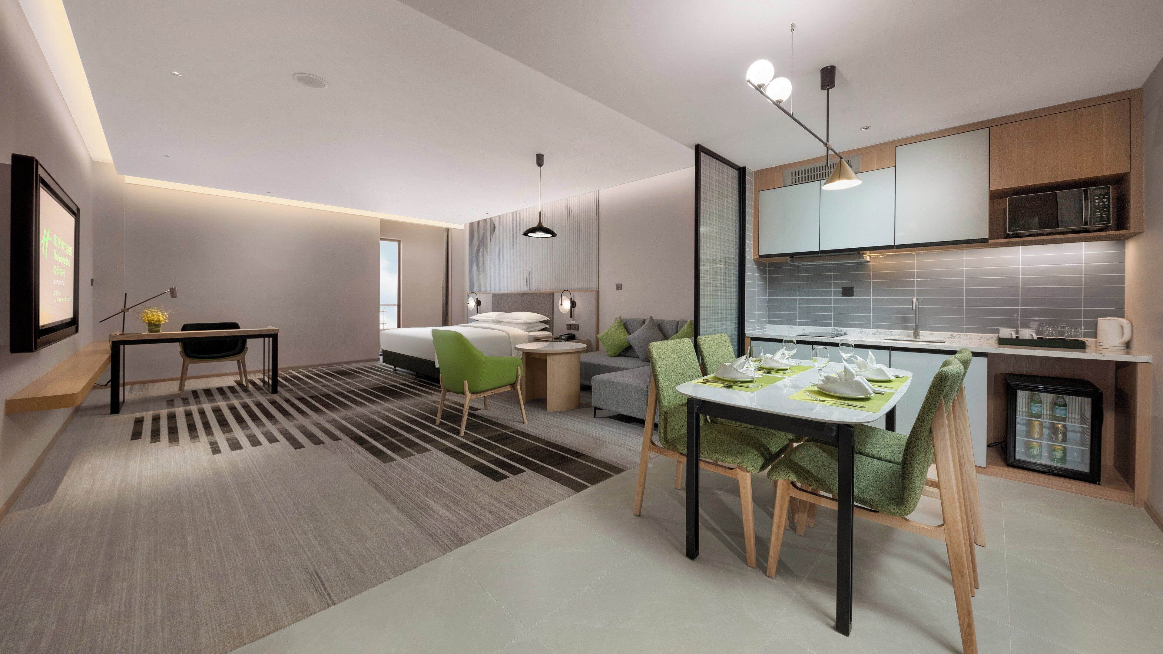 Een moderne hotelkamer met een bed, een zithoek met een bank en stoelen, een eettafel gedekt voor twee personen, en een kitchenette.