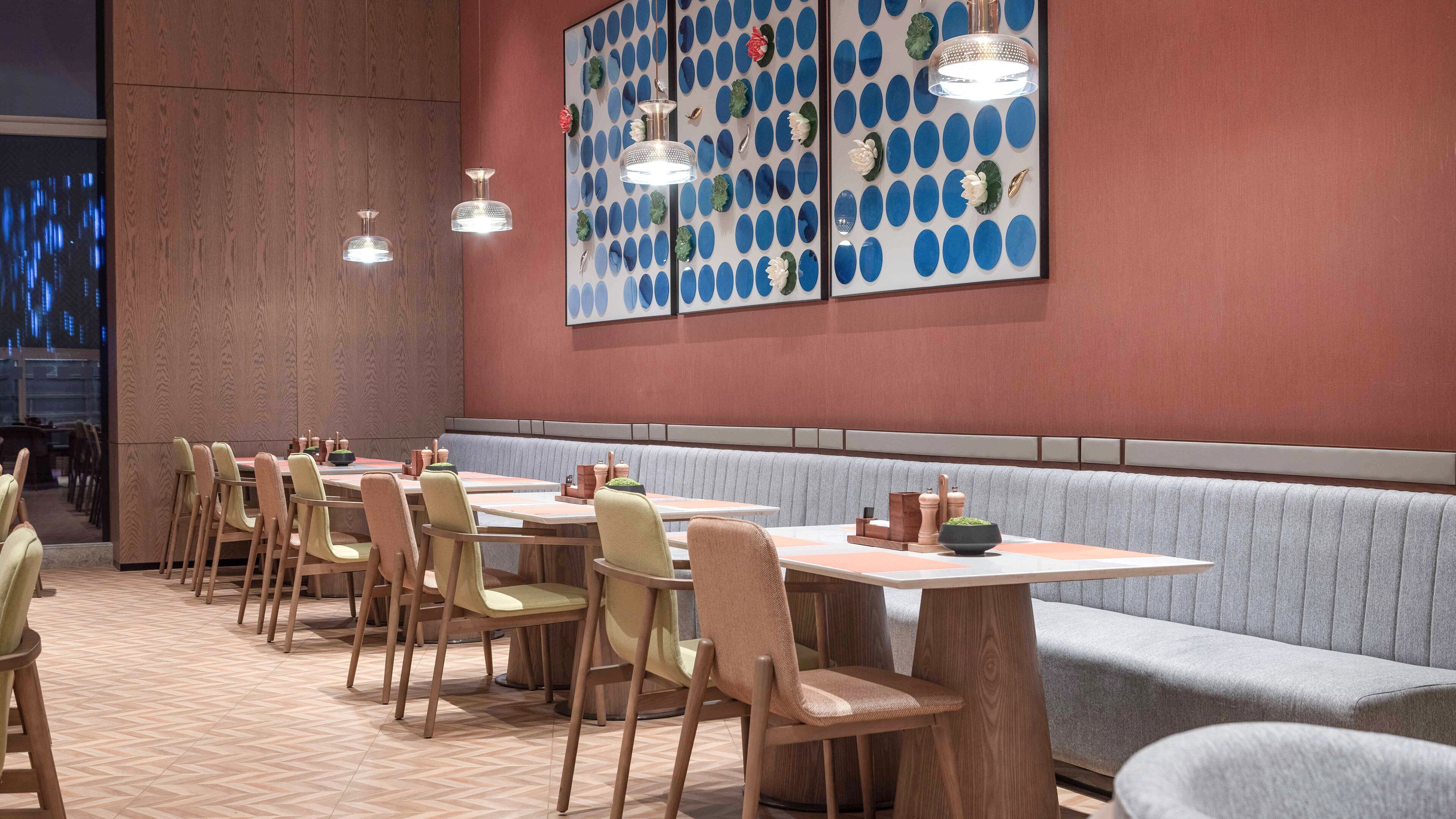 A restaurant with wooden tables and chairs, a patterned wall, and pendant lighting.