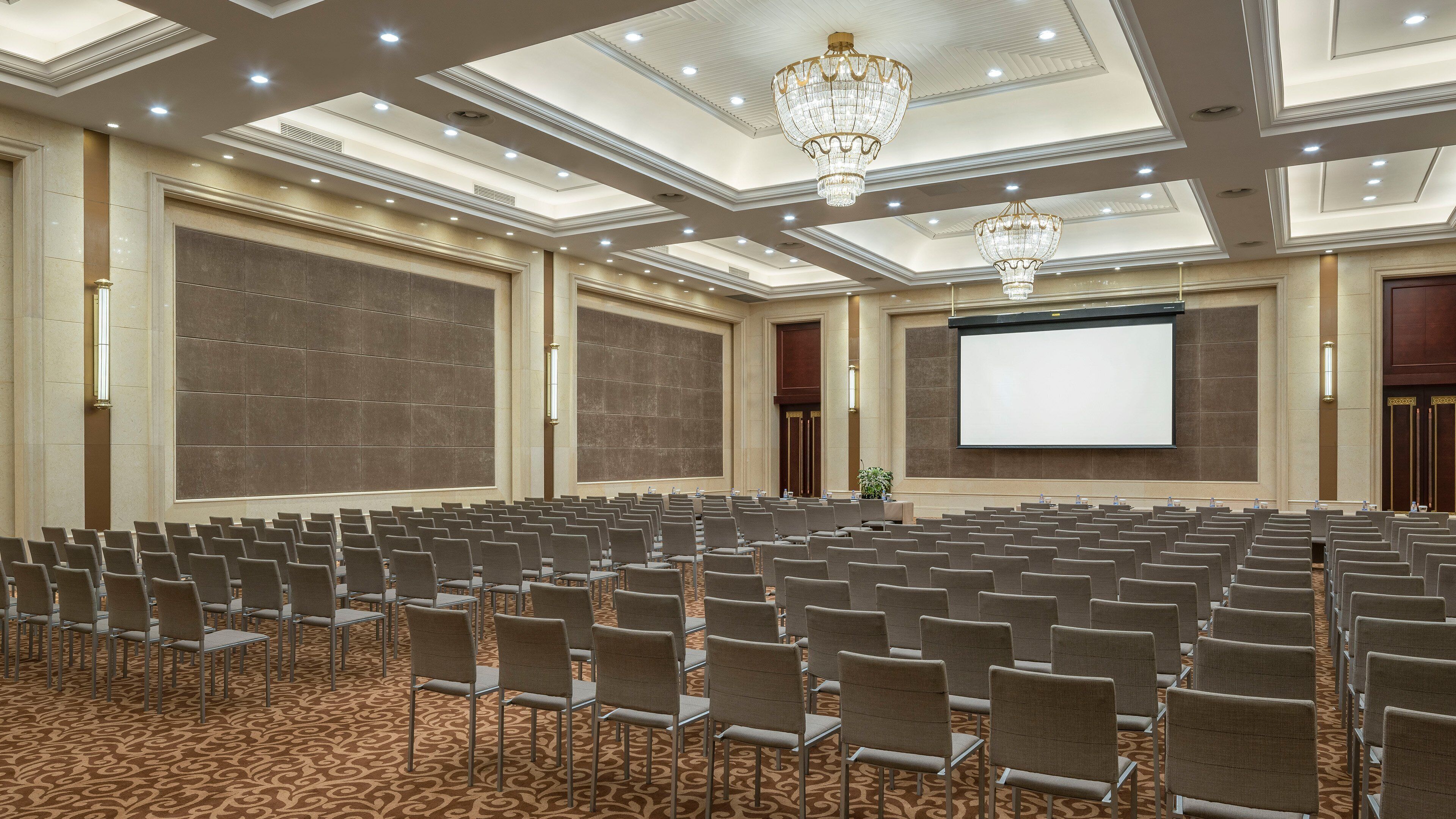 A conference room with rows of chairs, a large screen, and a chandelier.