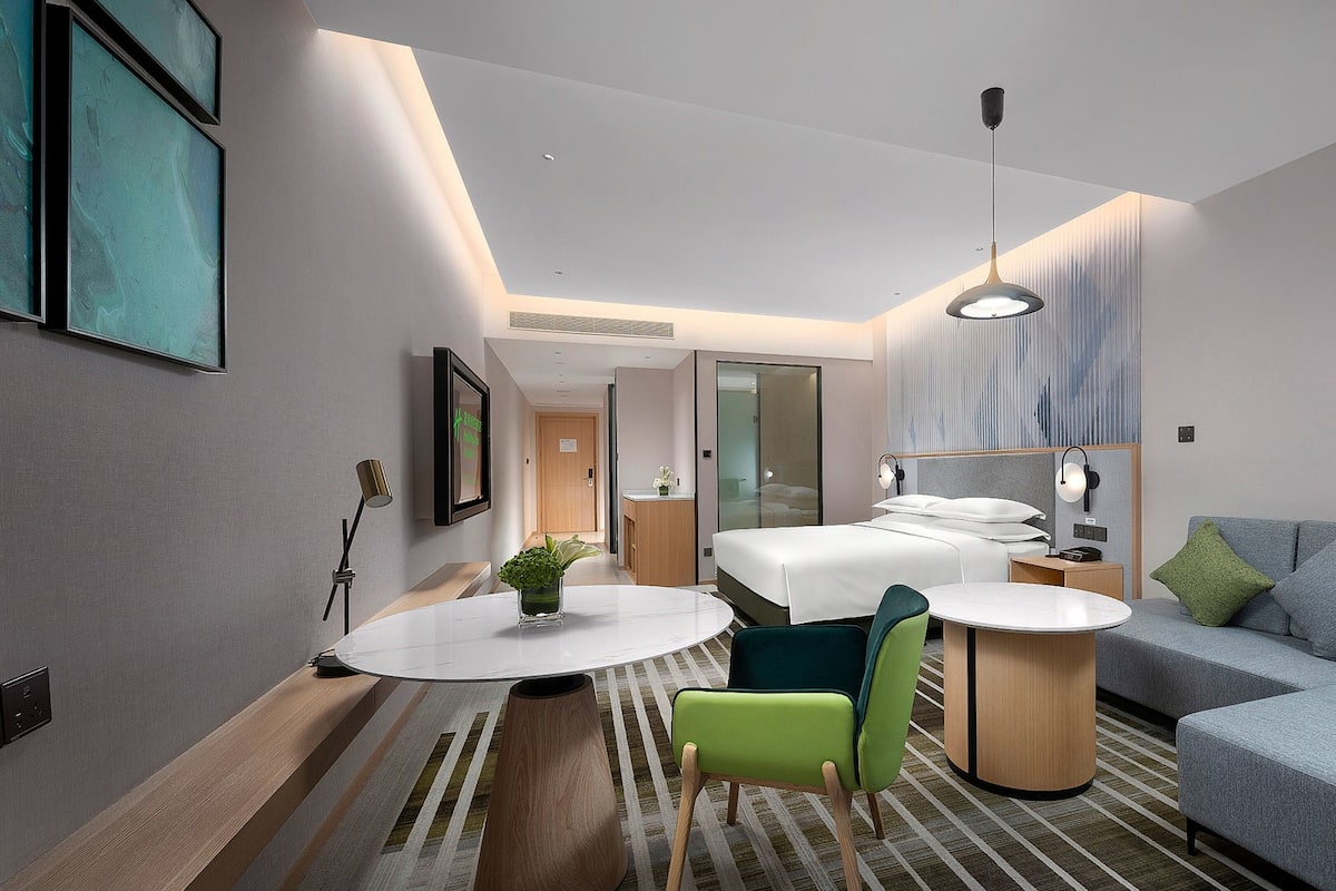 Una habitación de hotel moderna con cama, sofá, mesa de comedor y una pequeña cocina.
