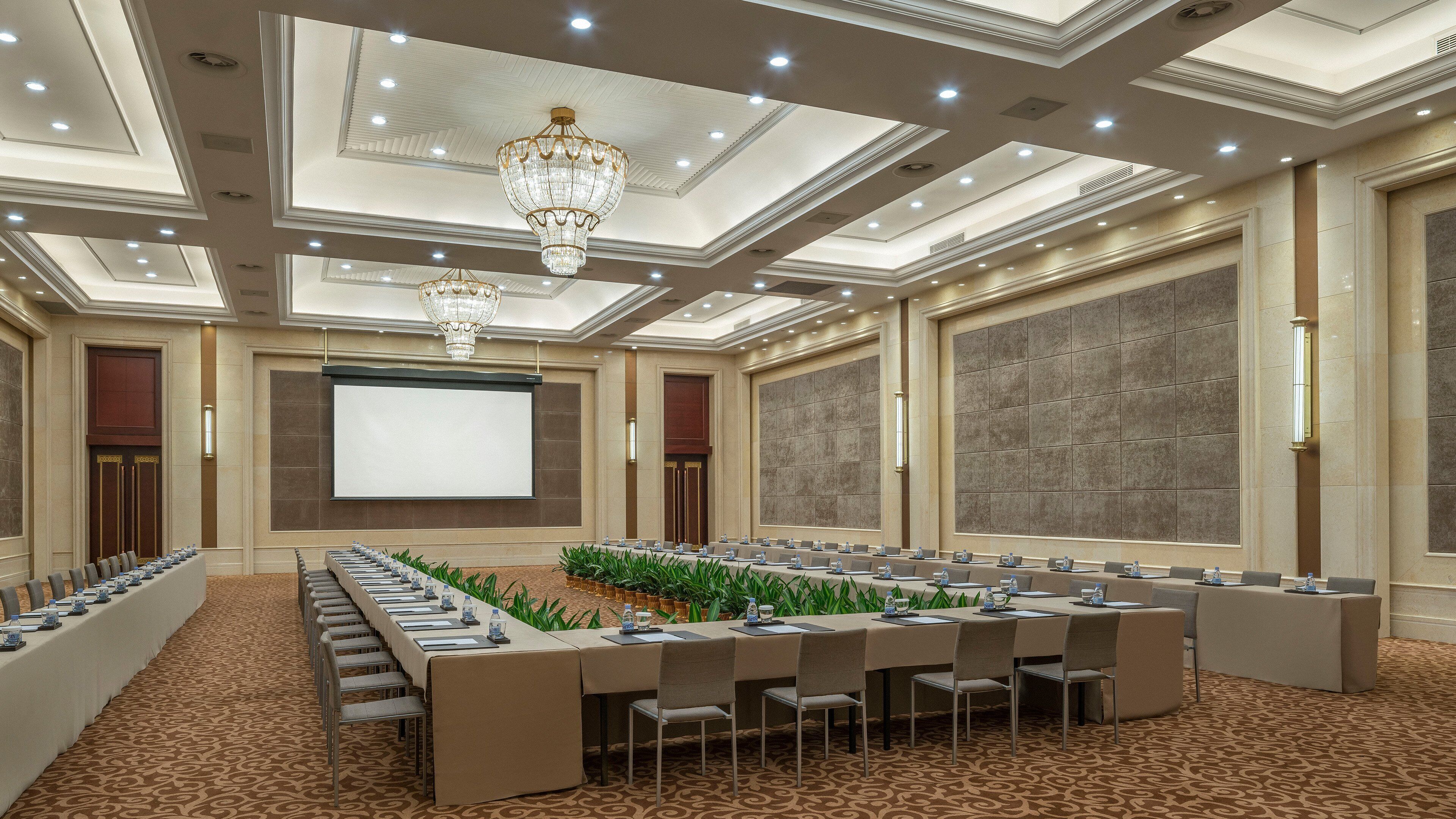 Un salón de conferencias con una larga mesa, sillas, una pantalla de proyector y una araña.