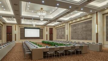 Un salón de conferencias con una larga mesa, sillas, una pantalla de proyector y una araña.