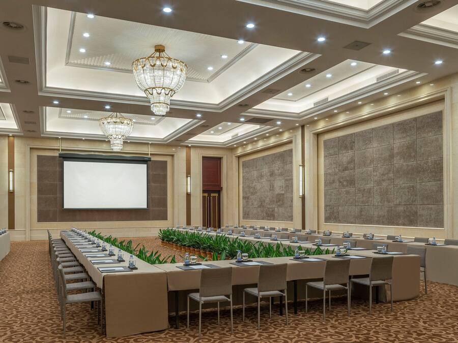 Un salón de conferencias con una larga mesa, sillas, una pantalla de proyector y una araña.