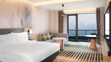 Habitación de hotel con una cama grande, un sofá, una mesita y un balcón con vistas a la ciudad.