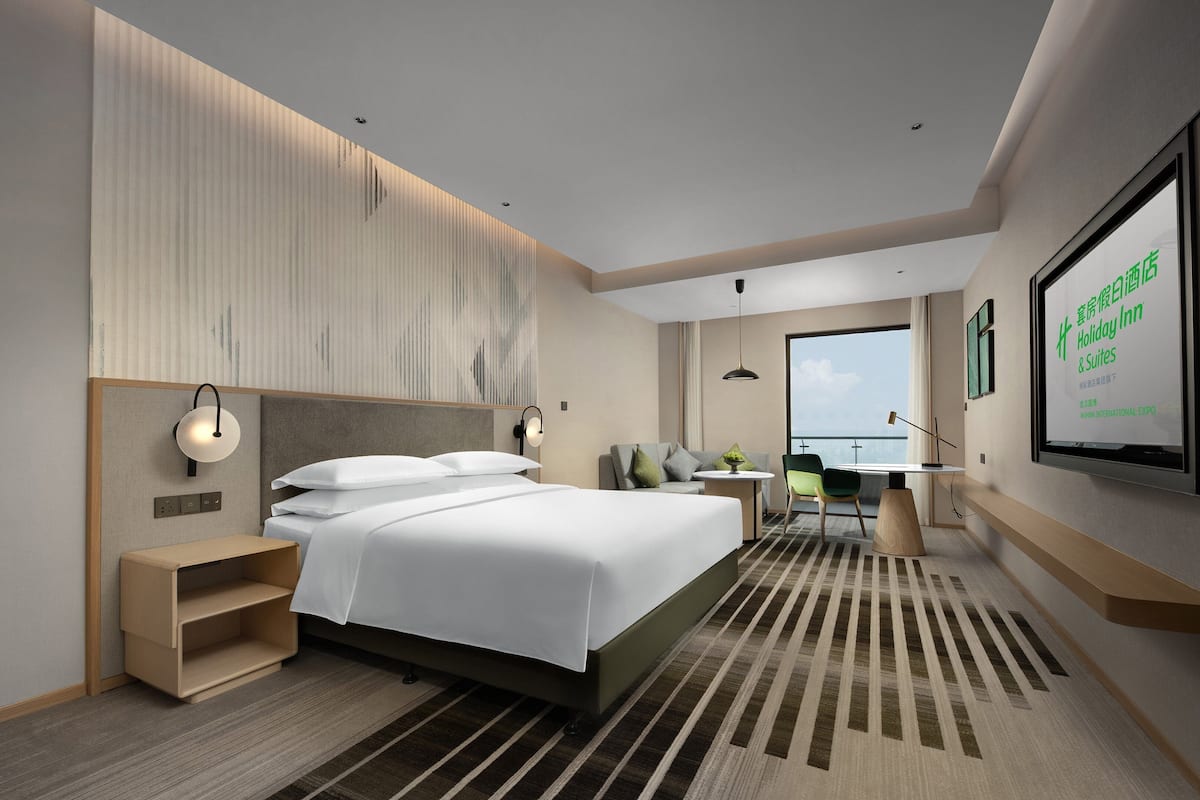 Una habitación de hotel moderna con una cama grande, mesitas de noche, un escritorio y vistas a la ciudad.