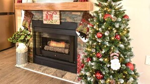 Una sala de estar con chimenea, un árbol de Navidad y un televisor colocado sobre la chimenea.