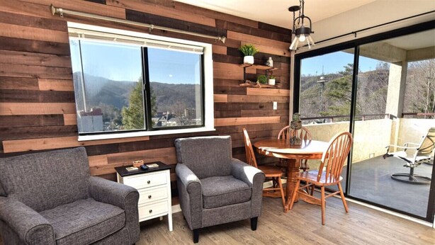 Una habitación moderna con pared de madera, un ventanal grande, una mesa de comedor con sillas y un balcón con una silla.