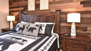 Un dormitorio con cabecera de madera, cama con ropa de cama estampada, dos lámparas de noche y una mesita de noche con un control remoto.