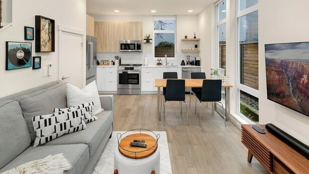 A modern kitchen with white cabinets, stainless steel appliances, and a dining area with a wooden table and chairs. - Stylish & cozy home w/ rooftop, space needle view! (Seattle)