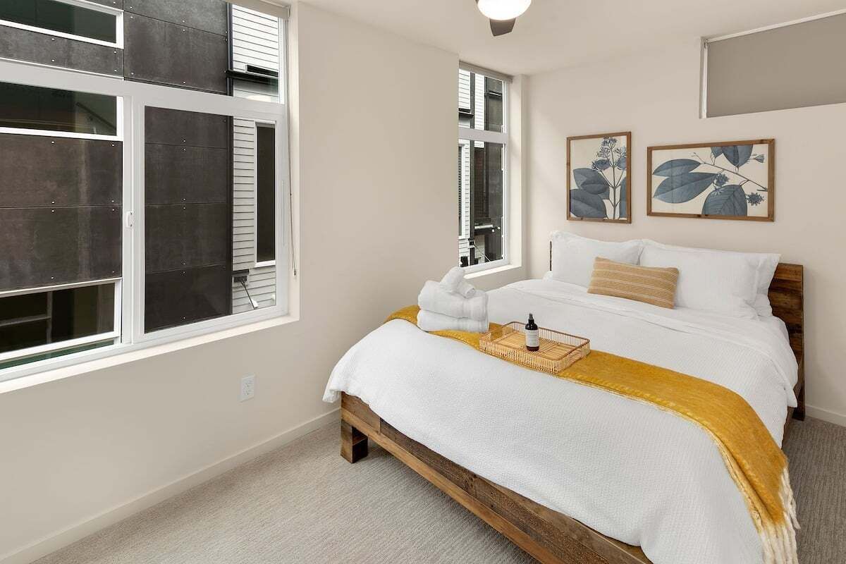 Un dormitorio con una cama, una ventana e impresiones enmarcadas de motivos botánicos en la pared.