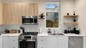 A modern kitchen with white cabinets, stainless steel appliances, and a window with a view of trees. - Stylish & cozy home w/ rooftop, space needle view! (Seattle)