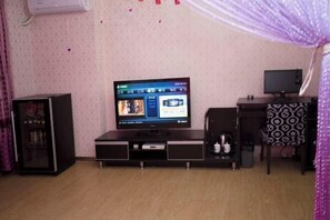 A room with a television on a stand, a small cabinet, a patterned chair, and a decorative curtain. - Huadu Modern Business Hotel (Jiaohe Boutique) (Jiaohe)