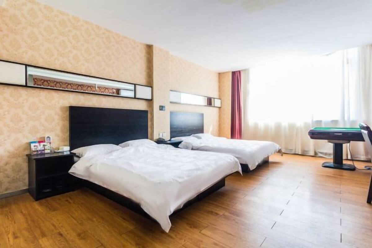 Ett hotellrum med två sängar, en platt-TV, ett litet skrivbord med en dator och ett fönster med gardiner.